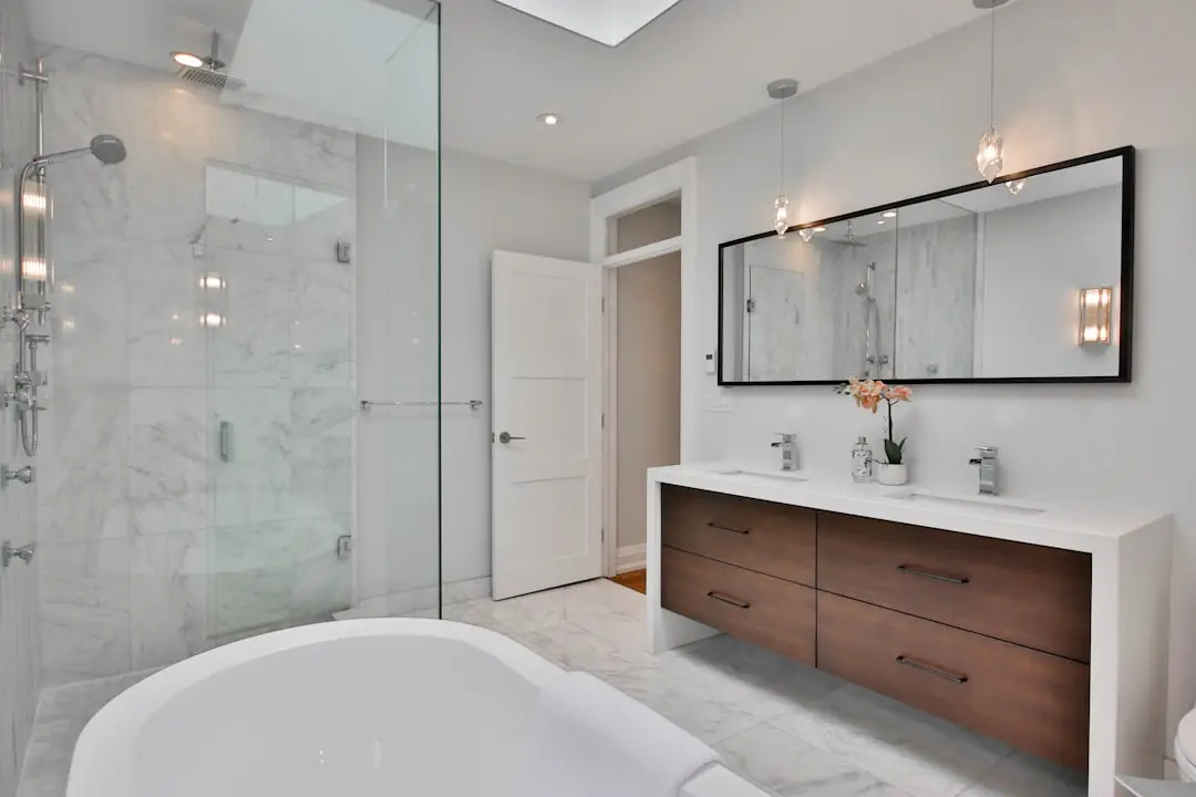 Modern bathroom with a glass-enclosed shower, freestanding tub, and a double-sink vanity with wood drawers