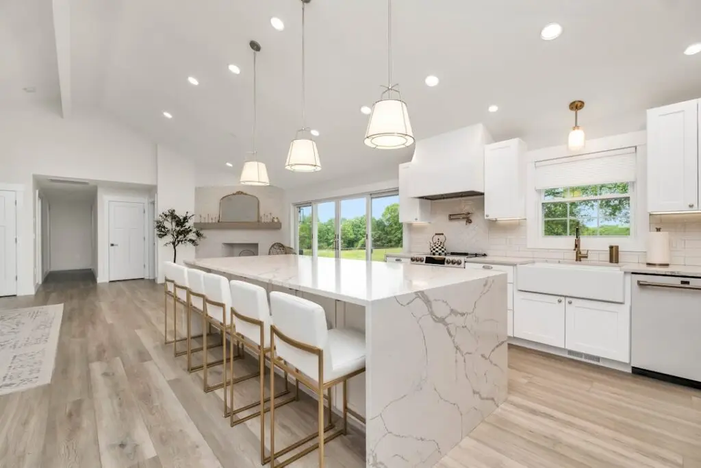 Bright, modern kitchen with a large marble island, white cabinets, and gold-bar stools lining the counter.