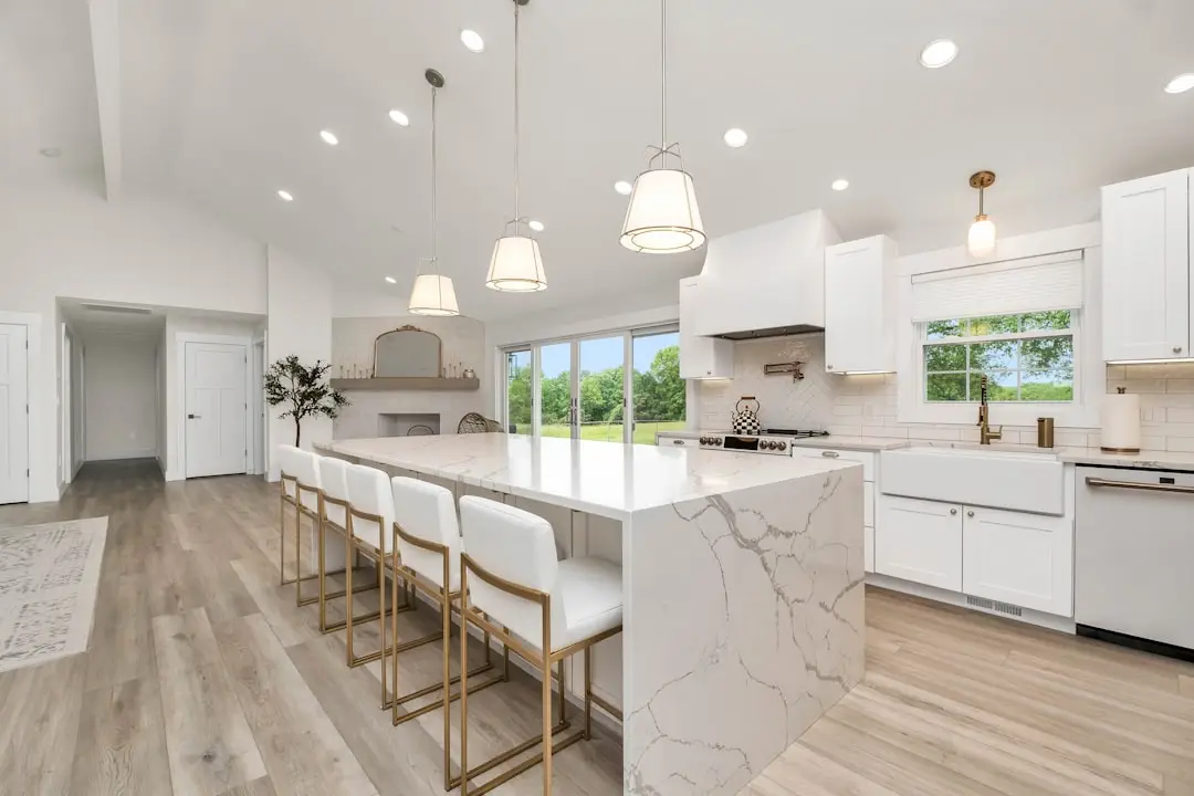 Bright, modern kitchen with a large marble island, white cabinets, and gold-bar stools lining the counter.
